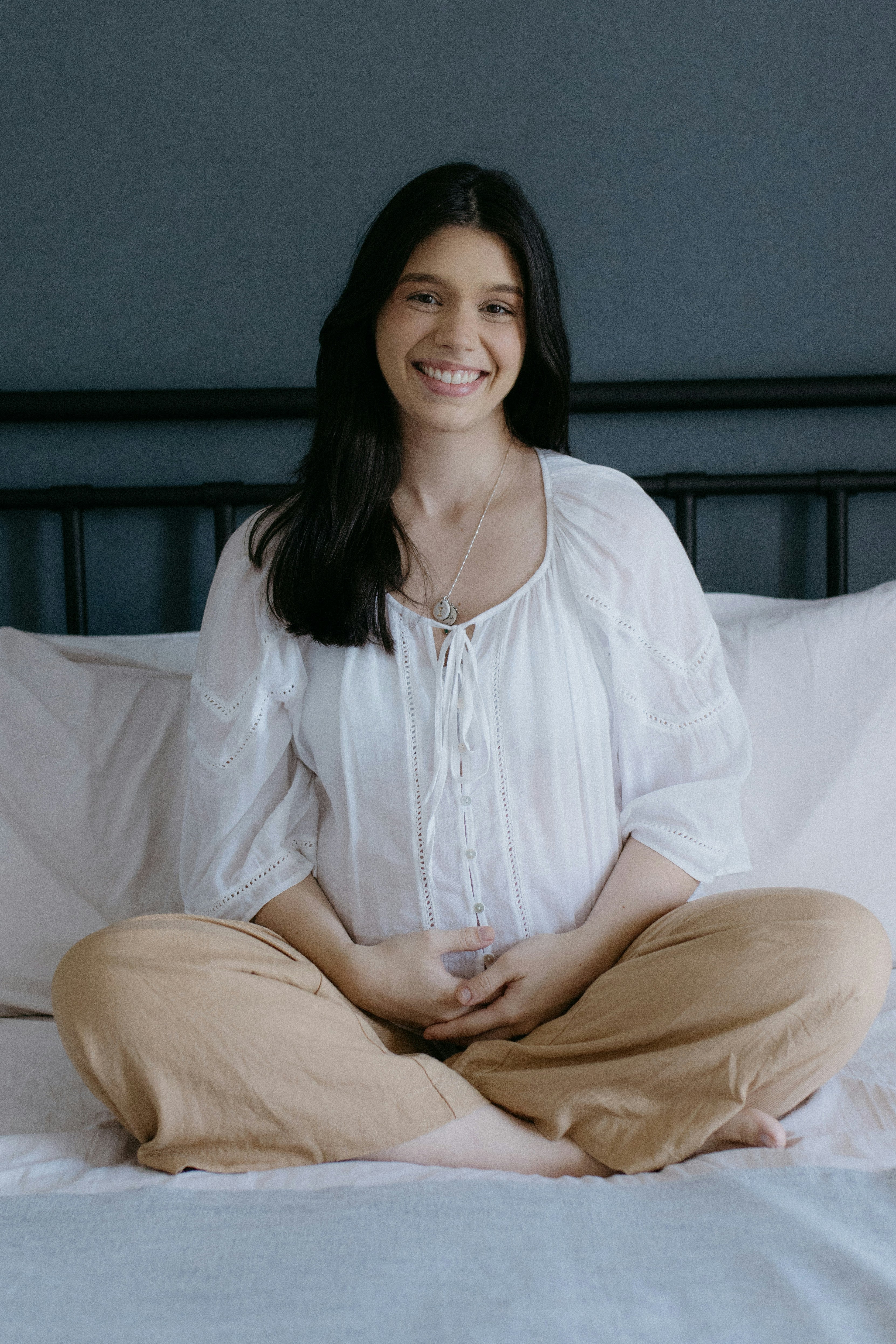 A woman sitting cross-legged on a bed, smiling